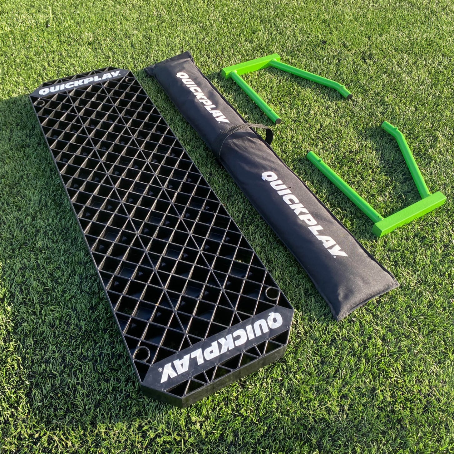 Onderdelen van de REPLAY Station XL op het gras: zwart bord, zwarte QUICKPLAY tas en twee groene frames.