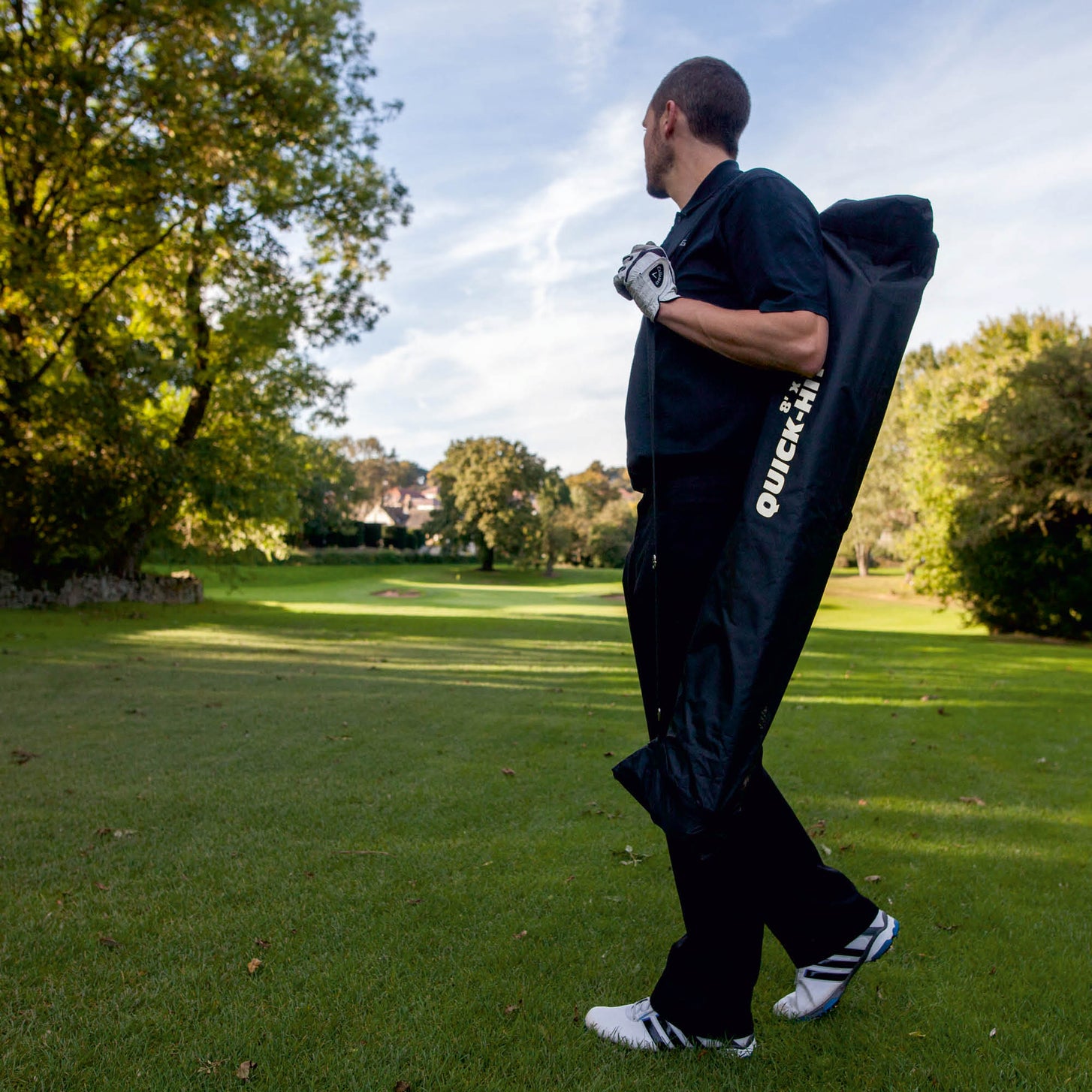 Golfer draagt het QUICK-HIT golfnet, verpakt in de zwarte QUICK-HIT tas, over zijn schouder op een golfbaan.