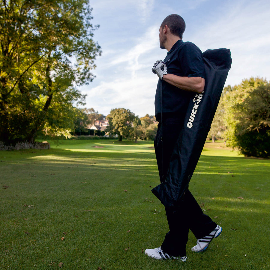 Golfer draagt het QUICK-HIT golfnet, verpakt in de zwarte QUICK-HIT tas, over zijn schouder op een golfbaan.