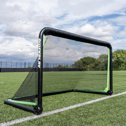 RHINO voetbaldoel 150 x 100 cm opgezet op een kunstgrasveld onder een bewolkte lucht, met bomen achter het hek.
