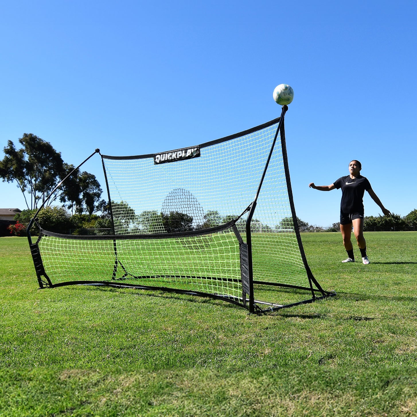 Speler wacht op een bal die omhoog kaatst van de TEKKERS Trainer voetbalrebounder met dubbel net op een grasveld.