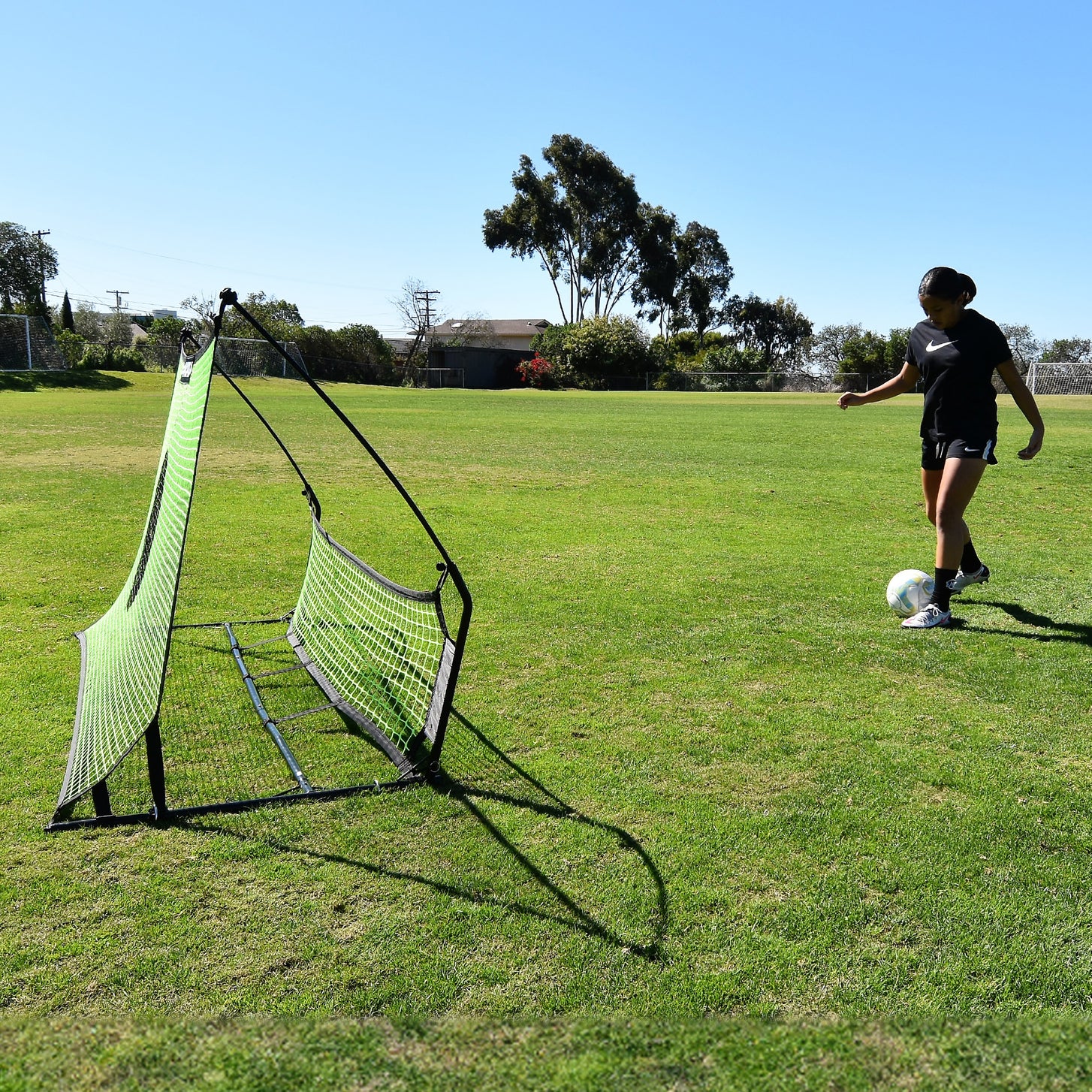 Speler staat op het punt een bal in de TEKKERS Trainer voetbalrebounder met dubbel net te spelen, van opzij gezien op het gras.
