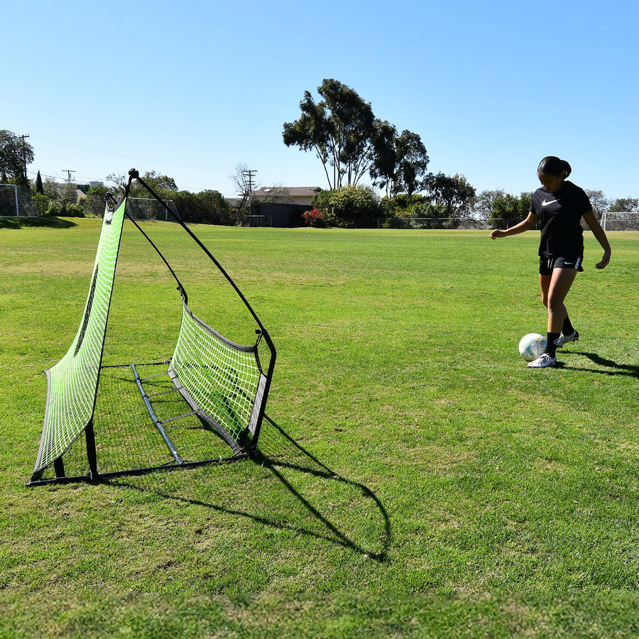 Speler staat op het punt een bal in de TEKKERS Trainer voetbalrebounder met dubbel net te spelen, van opzij gezien op het gras.