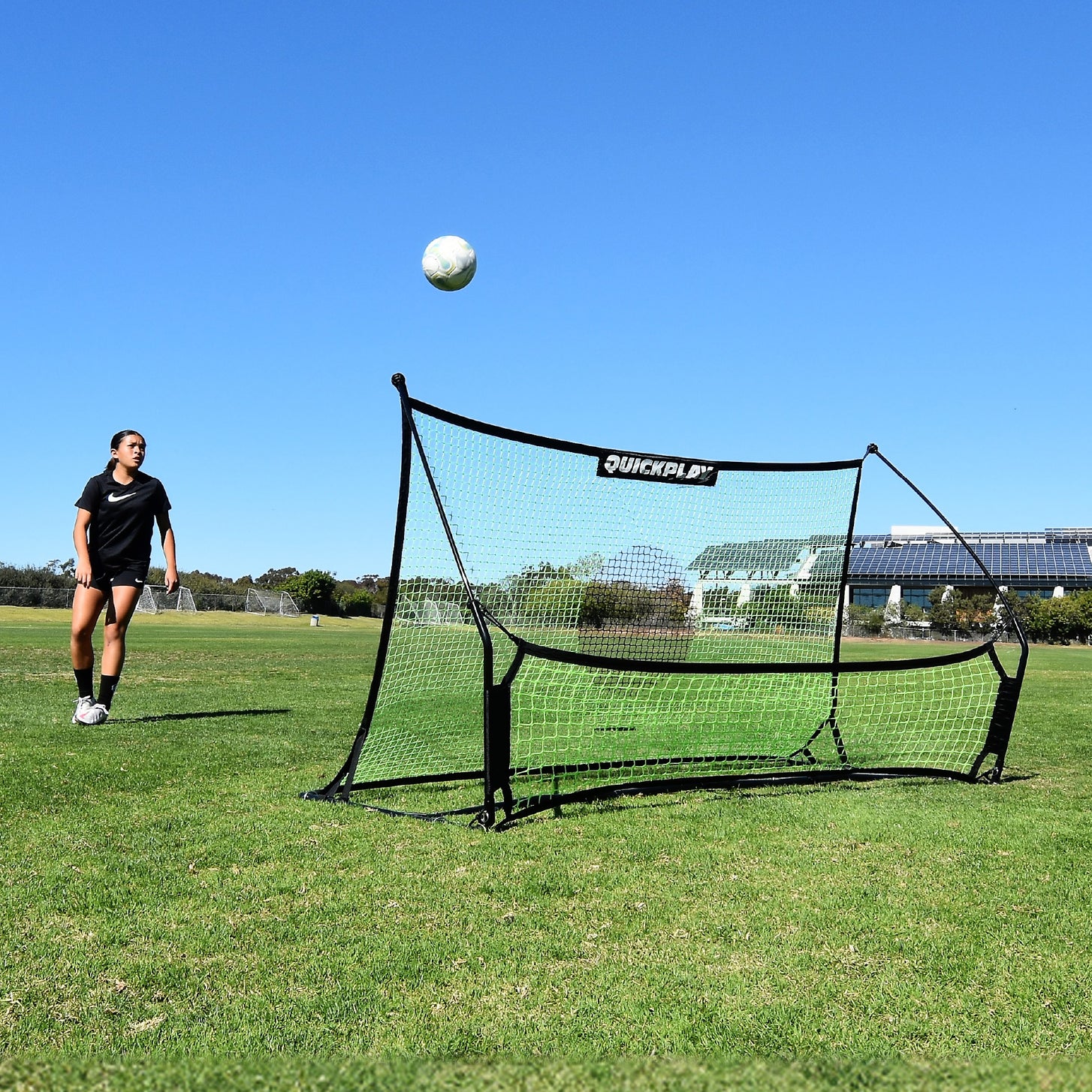 Speler kijkt hoe een bal omhoog komt van het net van de TEKKERS Trainer, vooraanzicht van de rebounder op een grasveld.