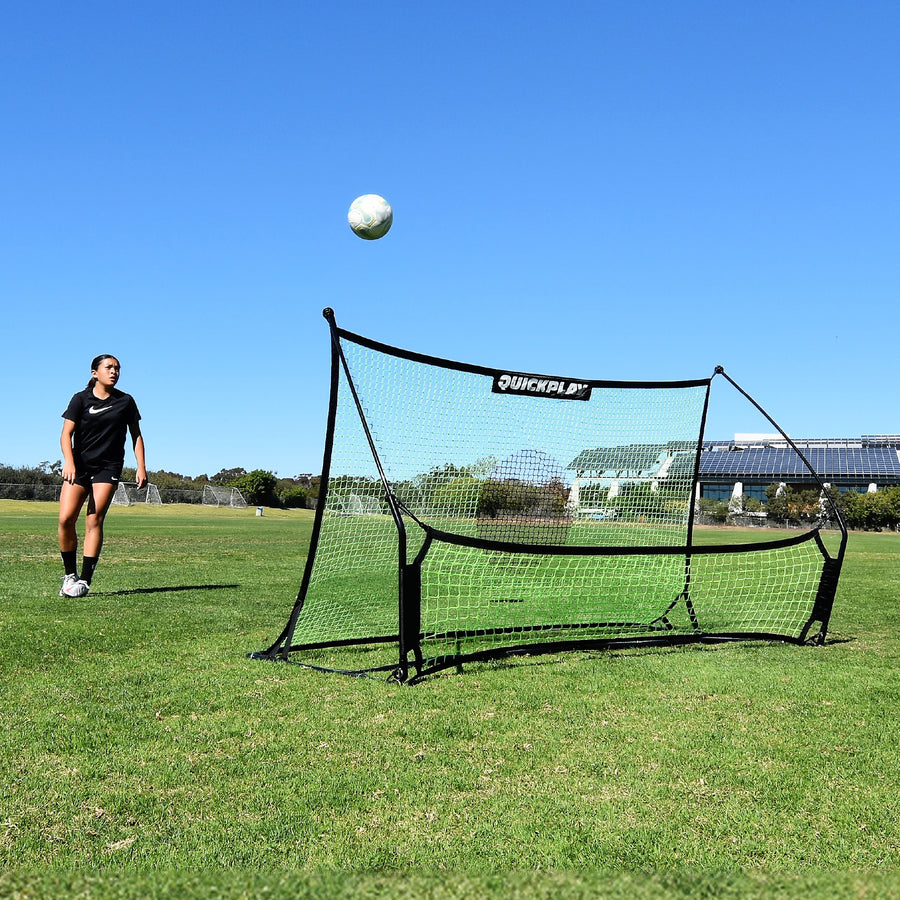 Speler kijkt hoe een bal omhoog komt van het net van de TEKKERS Trainer, vooraanzicht van de rebounder op een grasveld.